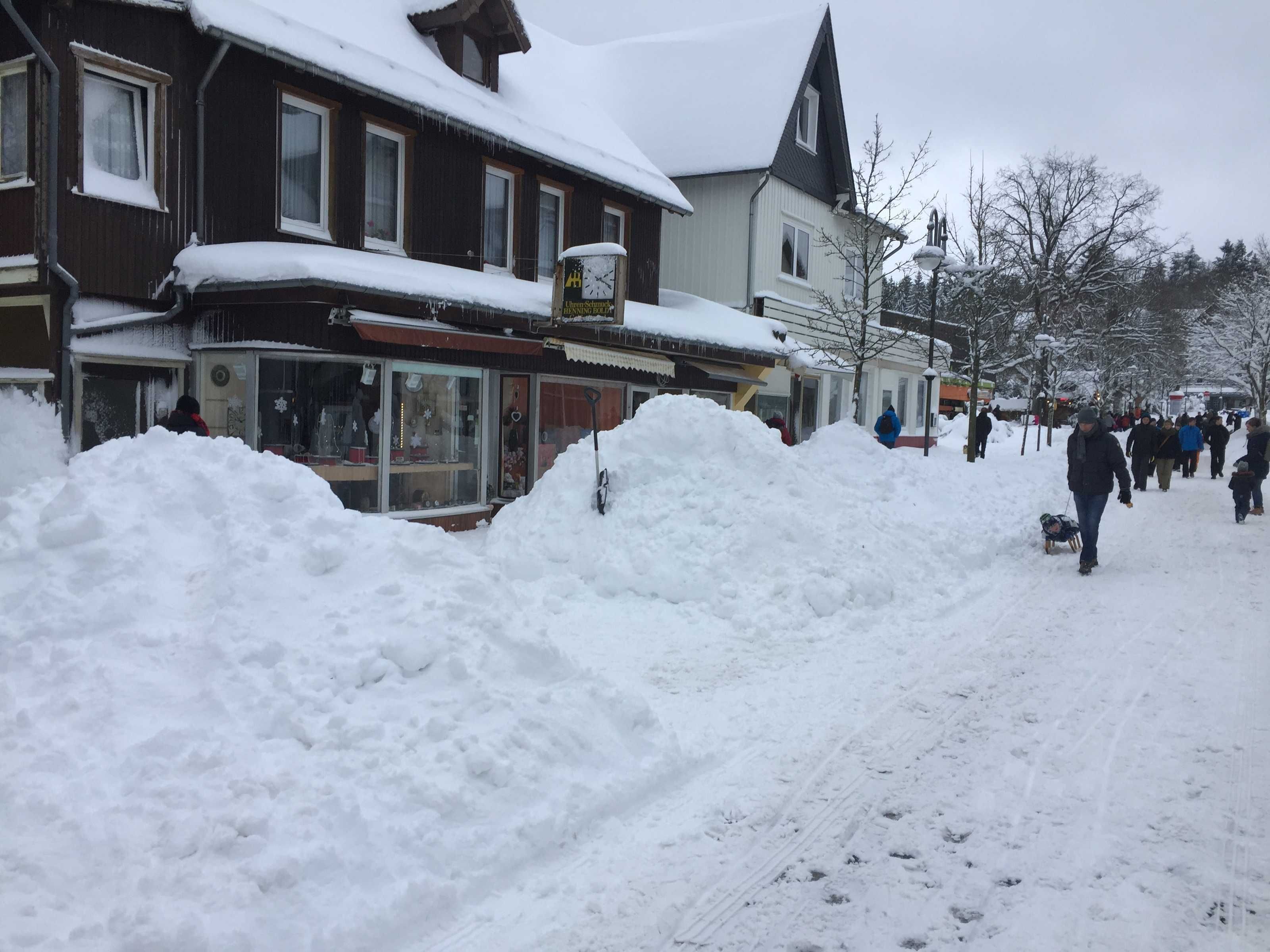 A snowy street with buildings and a pile of snow in the foreground.