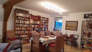 A cozy library with bookshelves, a dining table, wicker chairs, and a painting on the wall.