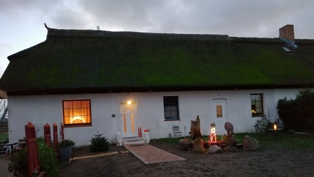 A white house with a thatched roof, a front door, and a small garden with a pathway leading to the entrance.