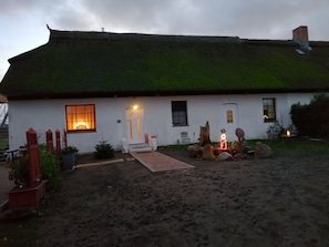 A white house with a thatched roof, a front door, and a small garden with a pathway leading to the entrance. - Haus am Peenebach, Germany (Klein Bünzow)