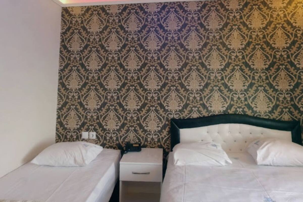 A room with two single beds, a nightstand, and a wall with a patterned wallpaper.