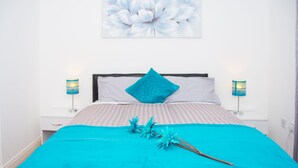 A neatly made bed with a blue blanket and decorative flowers, two bedside lamps, and a floral wall art piece. - Grand Central Friar Gate Deluxe (Derby)