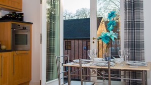 A kitchen with wooden cabinets, a built-in oven, and a dining table set for four with wine glasses and a vase of flowers. - Grand Central Friar Gate Deluxe (Derby)