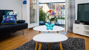 A modern living room with a black sofa, a white coffee table with a blue butterfly decoration, and a TV on a white cabinet. - Grand Central Friar Gate Deluxe (Derby)