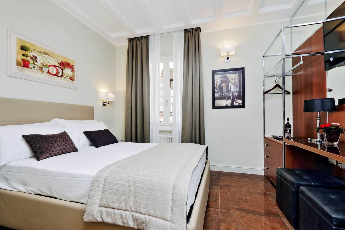A hotel room with a bed, a bedside table with a lamp, a mirror, a wardrobe, and a television.