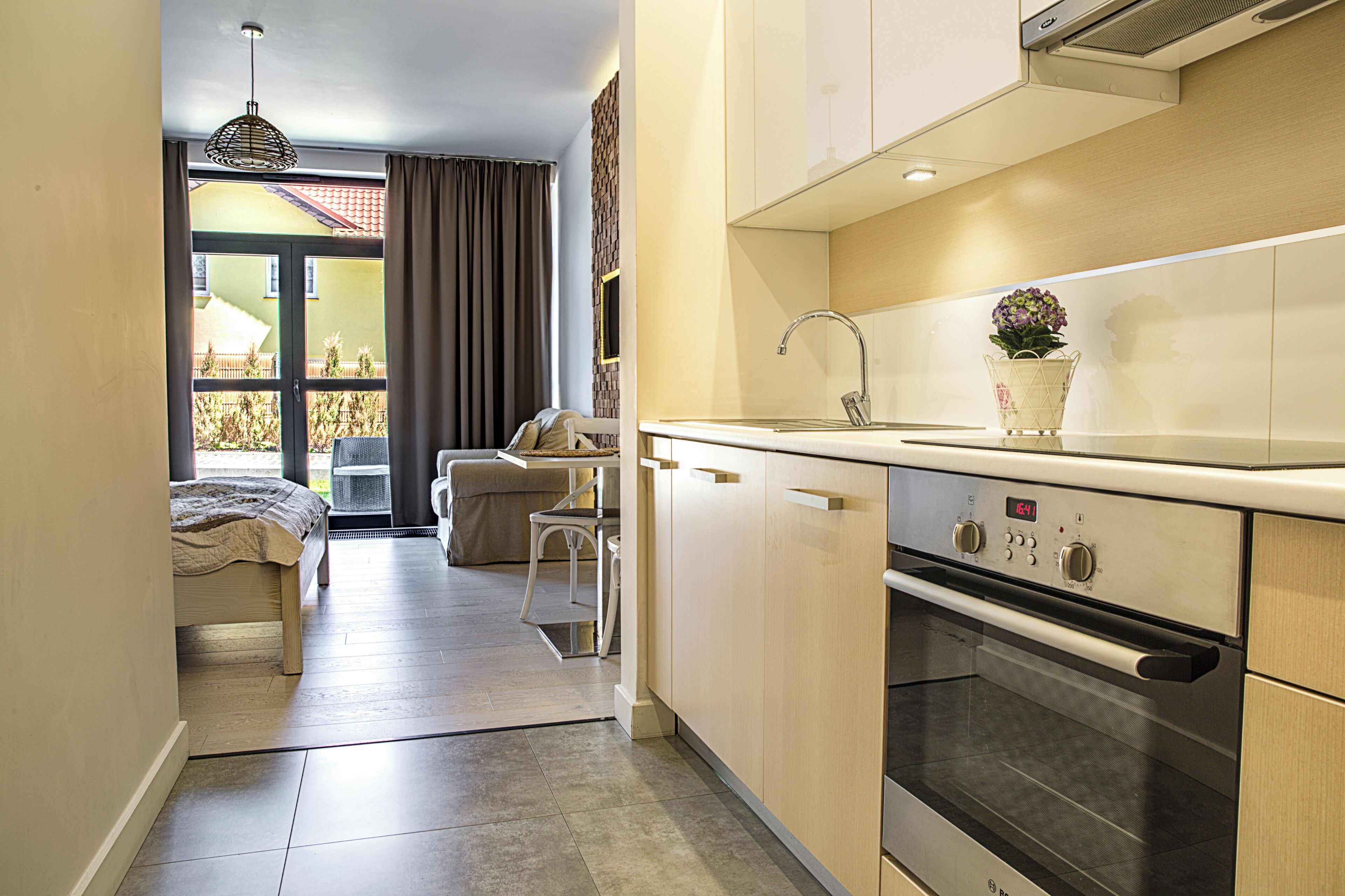 A compact kitchen with a built-in oven and a sink, a dining area with a table and chairs, and a view through a glass door to an outdoor balcony.
