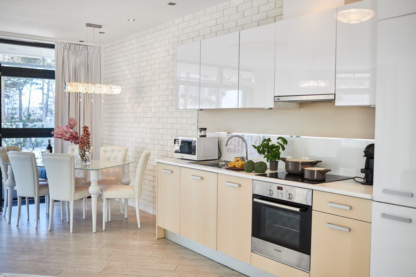A modern kitchen with white cabinets, a Bosch oven, a microwave, and a dining area with a glass table and white chairs.