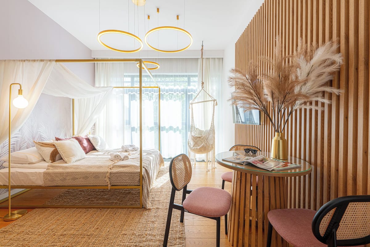 Un dormitorio moderno con una cama, una silla colgante, una mesa redonda y un panel decorativo en la pared.