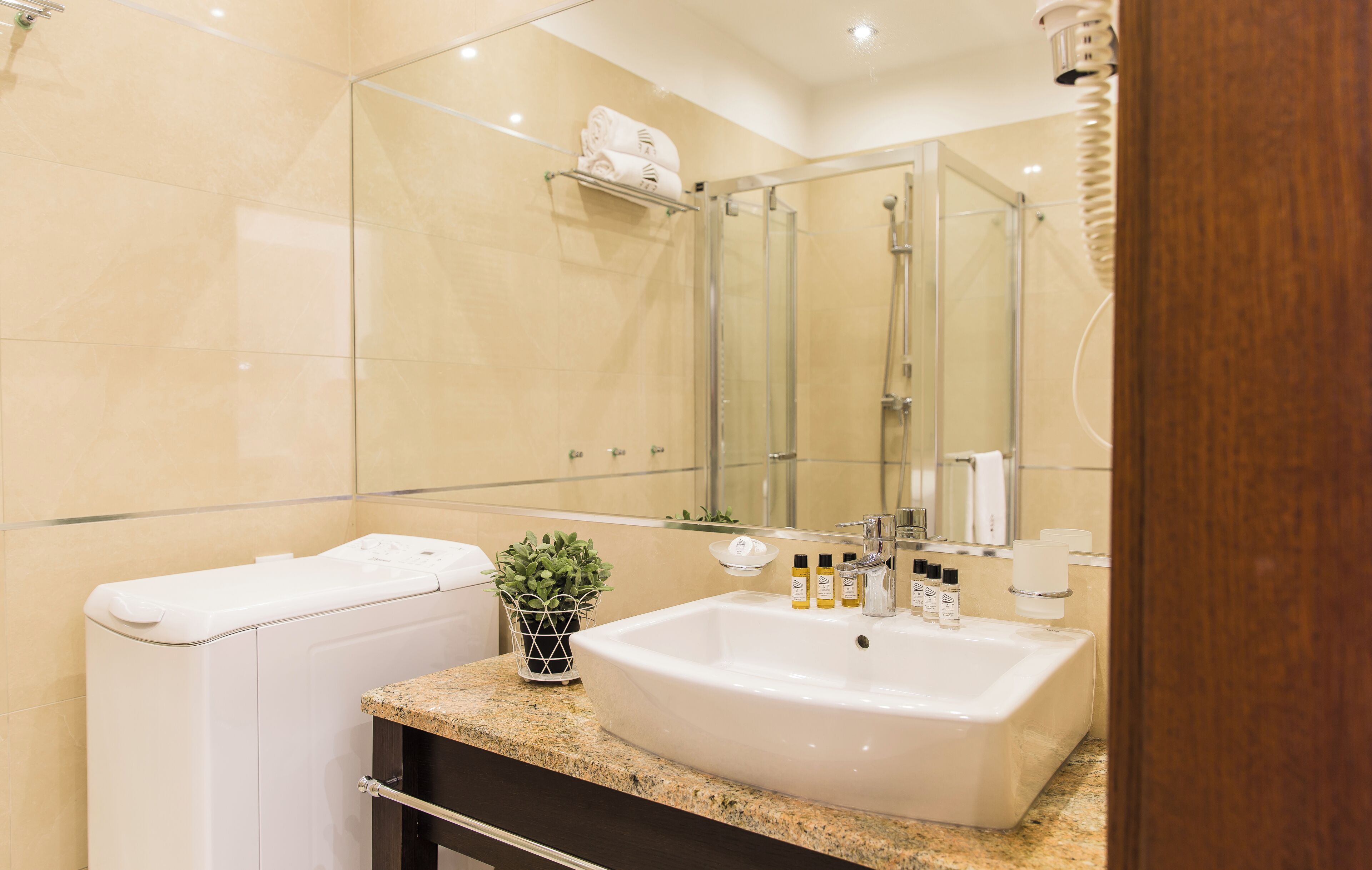 Un baño moderno con un espejo grande, un lavamanos blanco, una cabina de ducha de cristal y un inodoro.