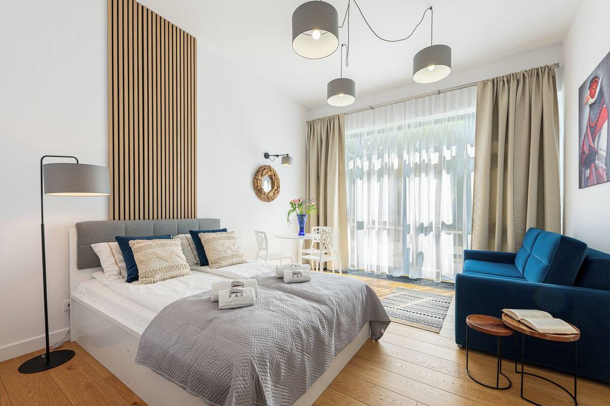 Un dormitorio moderno con cama, un sofá azul, una mesita y una lámpara de pie.