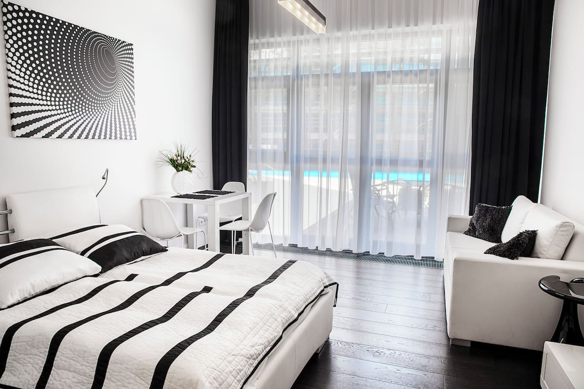 Una habitación de hotel moderna con una cama grande, un escritorio y un sofá. Se ve una piscina a través de la ventana.