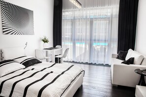 Una habitación de hotel moderna con una cama grande, un escritorio y un sofá. Se ve una piscina a través de la ventana.