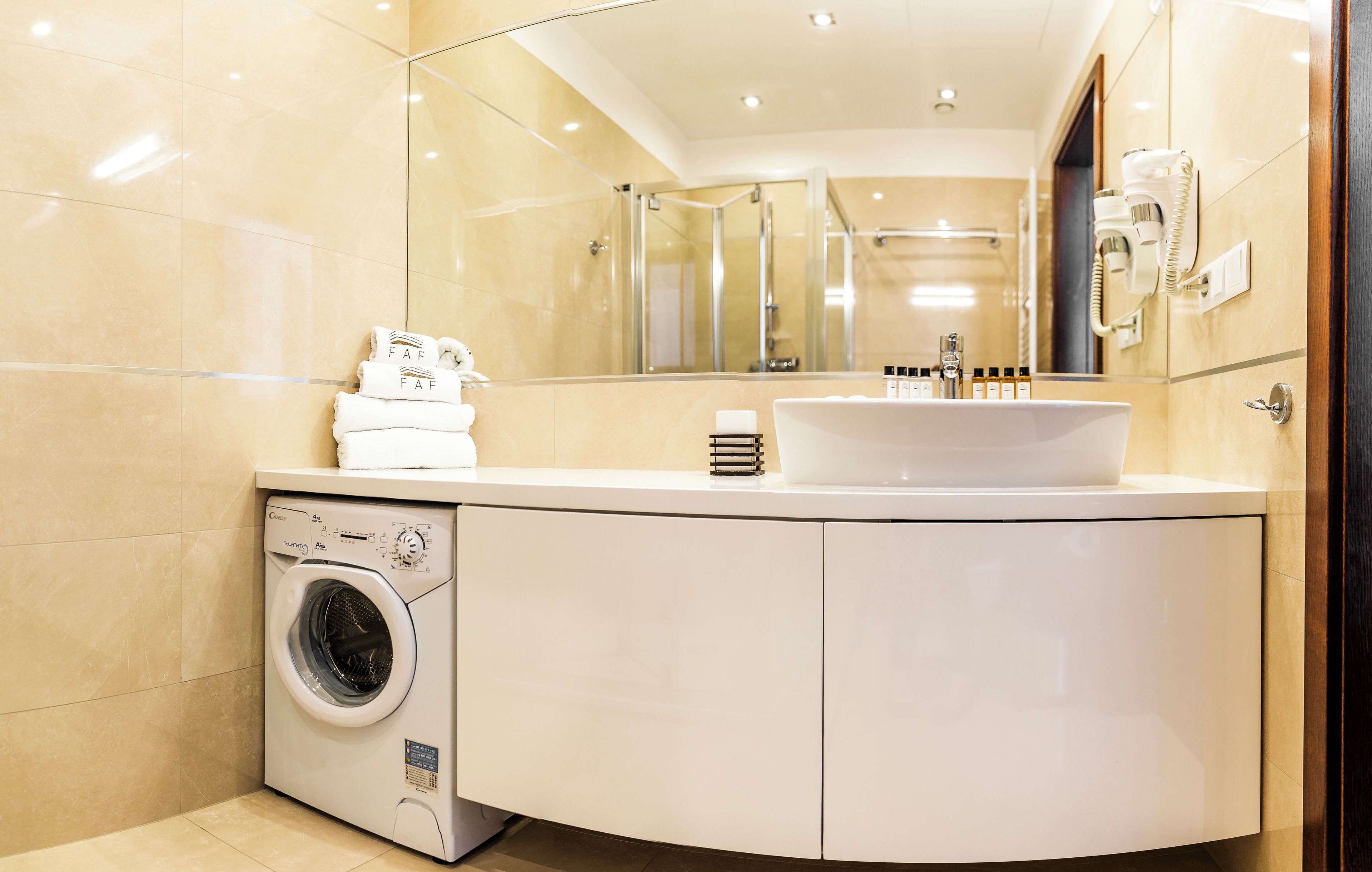 Un baño moderno con lavadora integrada, un lavabo con artículos de aseo y un espejo grande.