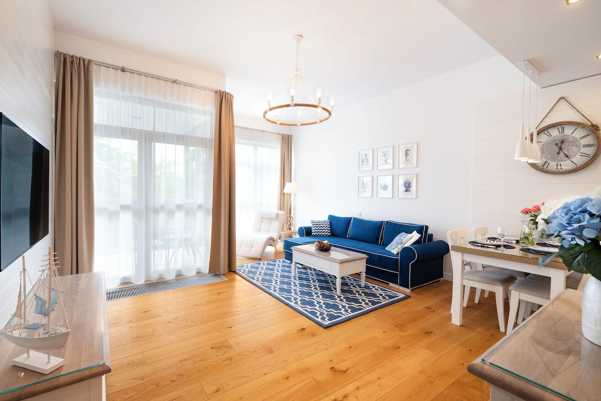 Una sala moderna con un sofá azul, una mesa de centro de madera y una mesa de comedor preparada para cuatro comensales.
