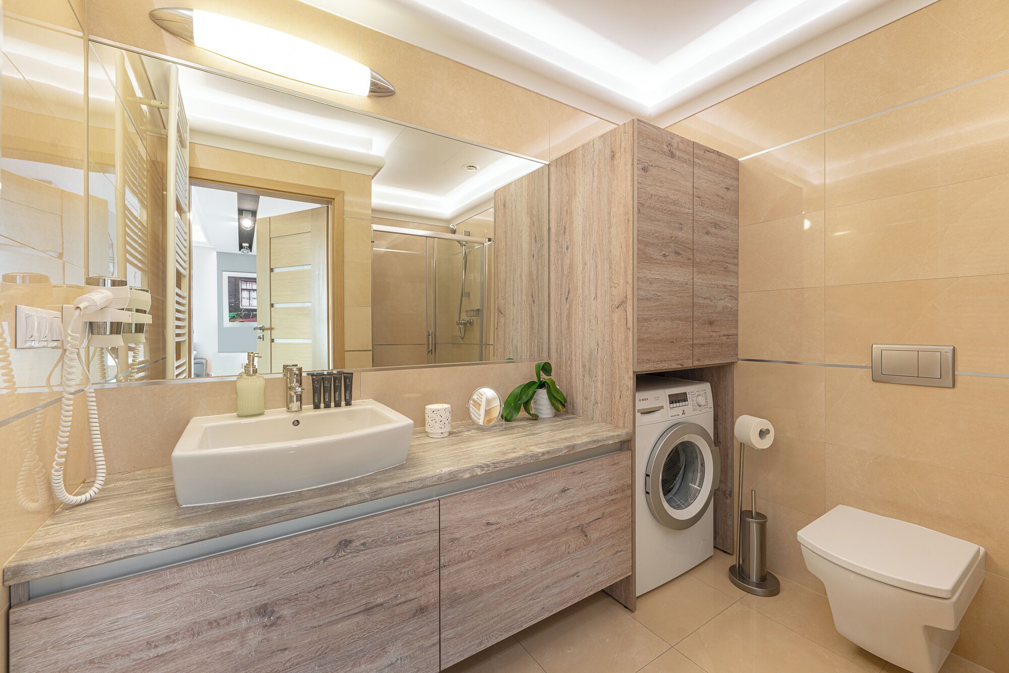 A modern bathroom with a sink, mirror, and a washing machine.