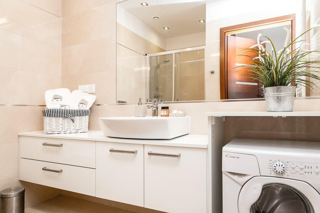Un baño moderno con un lavamanos blanco, un espejo, una ducha y una lavadora integrada.