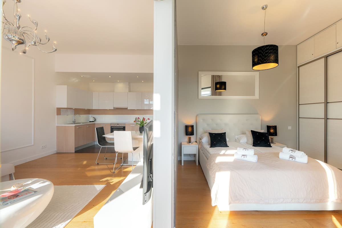Una habitación de hotel moderna con una cama grande, una zona de estar separada con una silla y una mesa, una kitchenette y un baño.