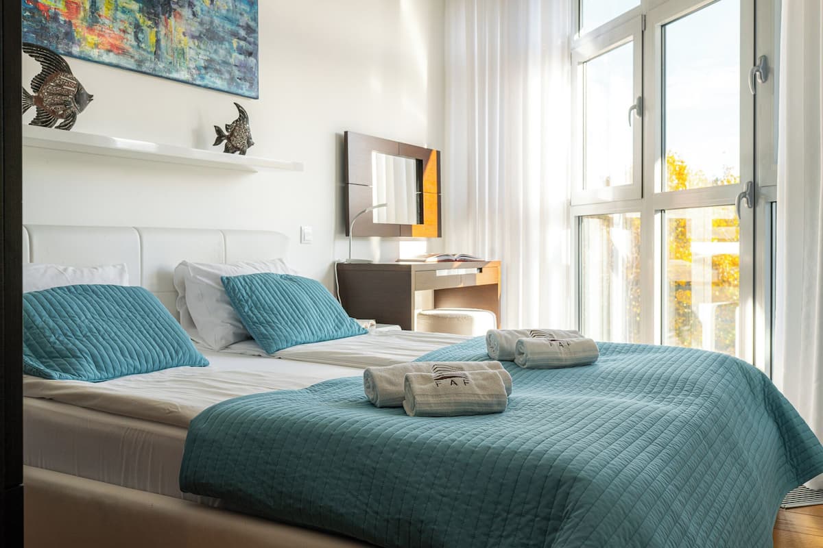 Una habitación de hotel moderna con una cama grande, dos almohadas, una mesita de noche, un espejo y vistas al exterior.