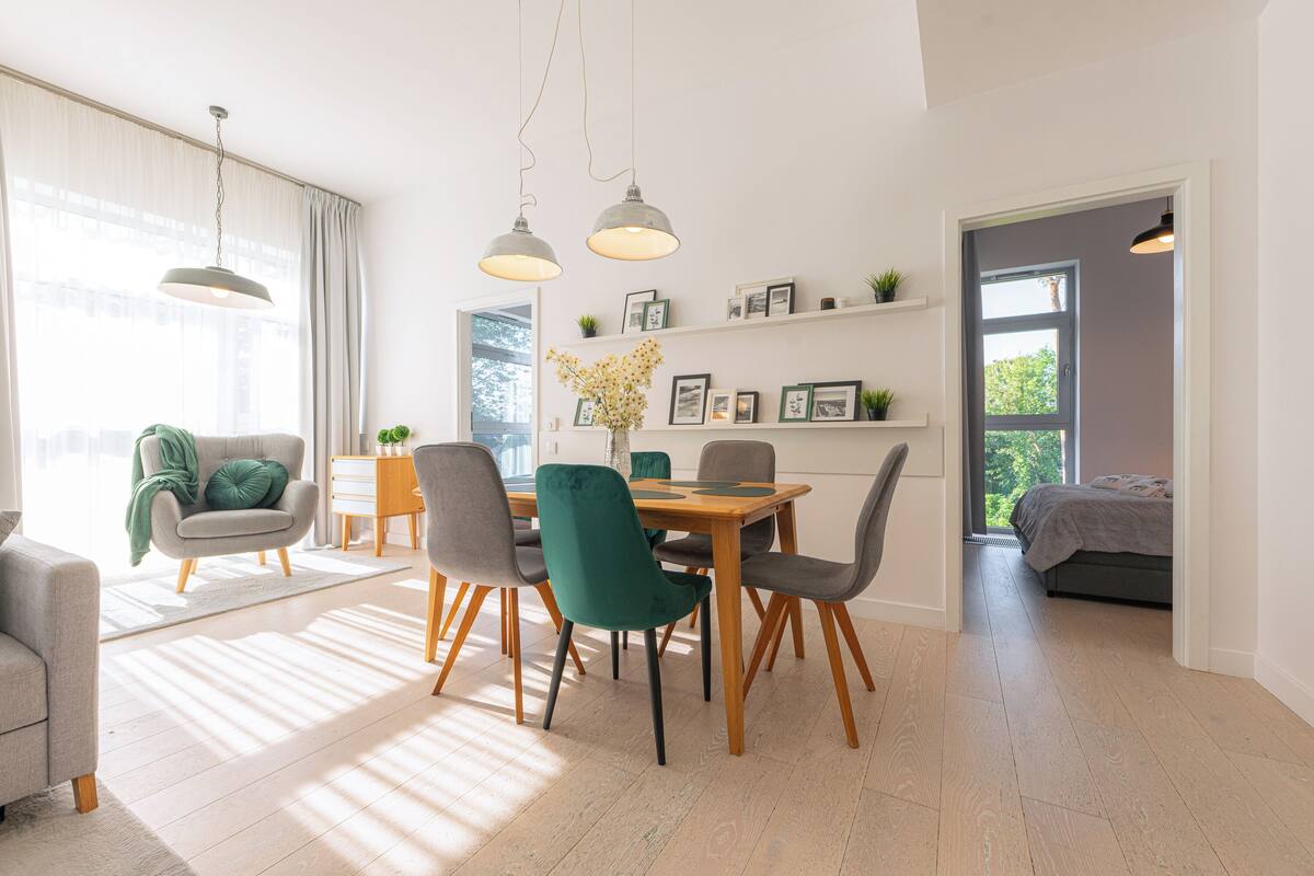 Un comedor moderno con una mesa y sillas de madera, un jarrón de flores y vistas al exterior a través de un amplio ventanal.