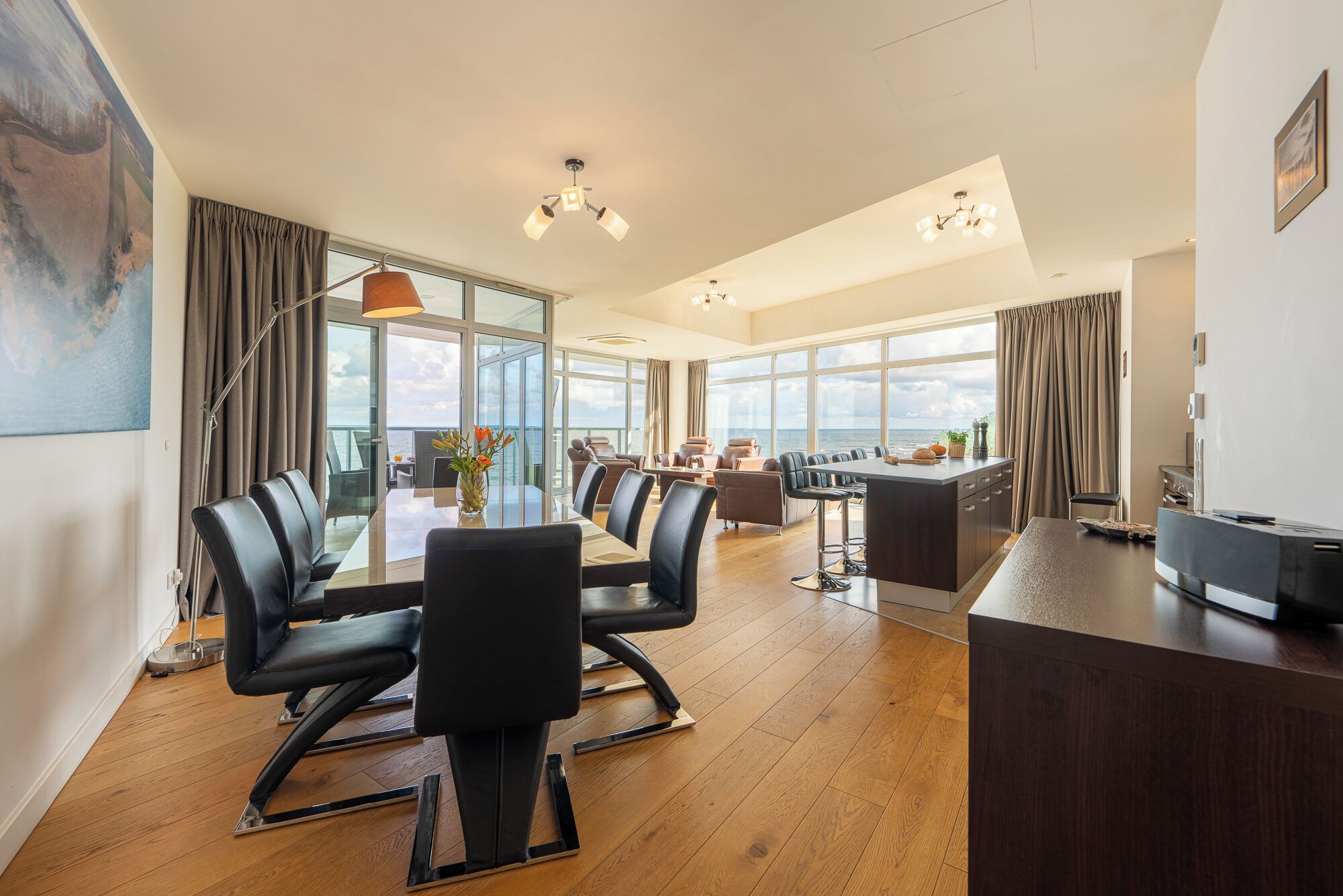 Amplia habitación con una gran mesa de comedor, asientos cómodos, zona de cocina y grandes ventanales con vistas al mar.