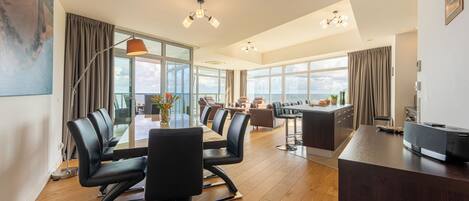 Amplia habitación con una gran mesa de comedor, asientos cómodos, zona de cocina y grandes ventanales con vistas al mar.