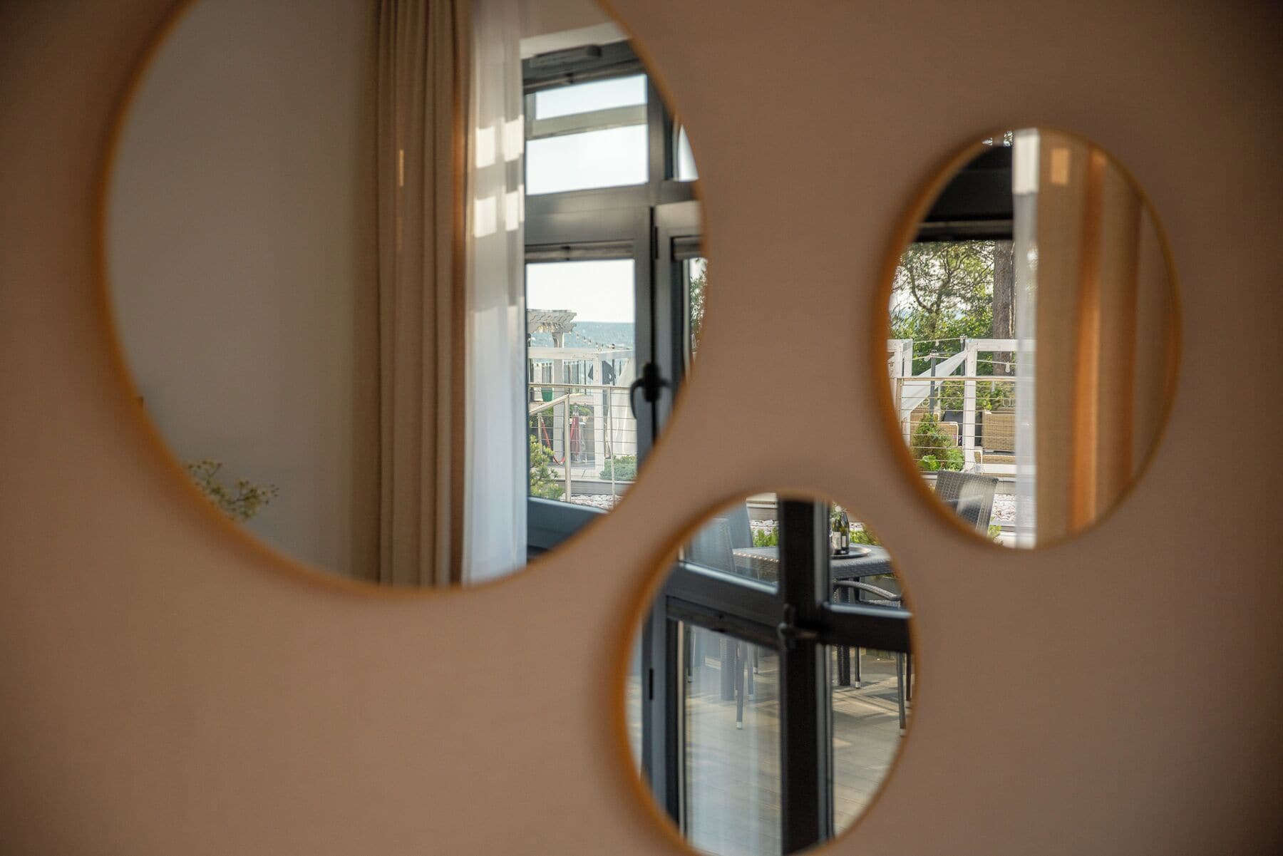 A view through circular cutouts in a wall, revealing a balcony with outdoor furniture and a railing.