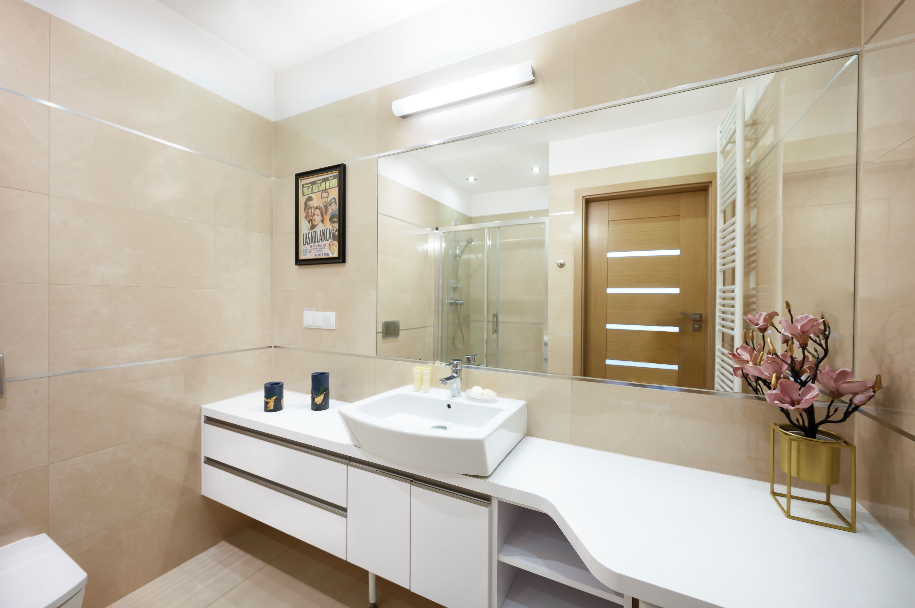 A modern bathroom with a large mirror, a white sink, and a vanity with drawers.