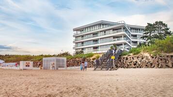 Un hotel frente a la playa con diseño moderno, que cuenta con varios balcones y una escalera que conduce a los niveles superiores.