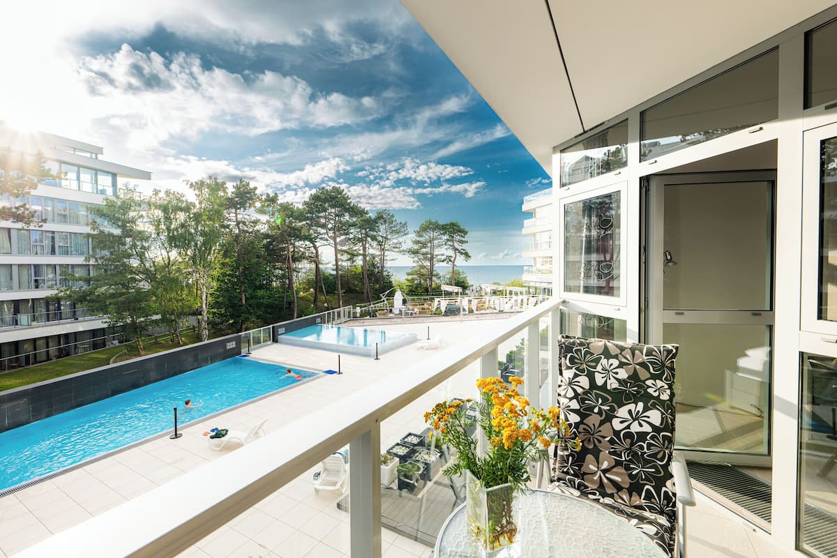 Un balcón con vistas a una piscina, una puerta de cristal y una silla estampada con motivos florales.