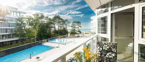 A balcony with a view of a swimming pool, a glass door, and a chair with a floral pattern.