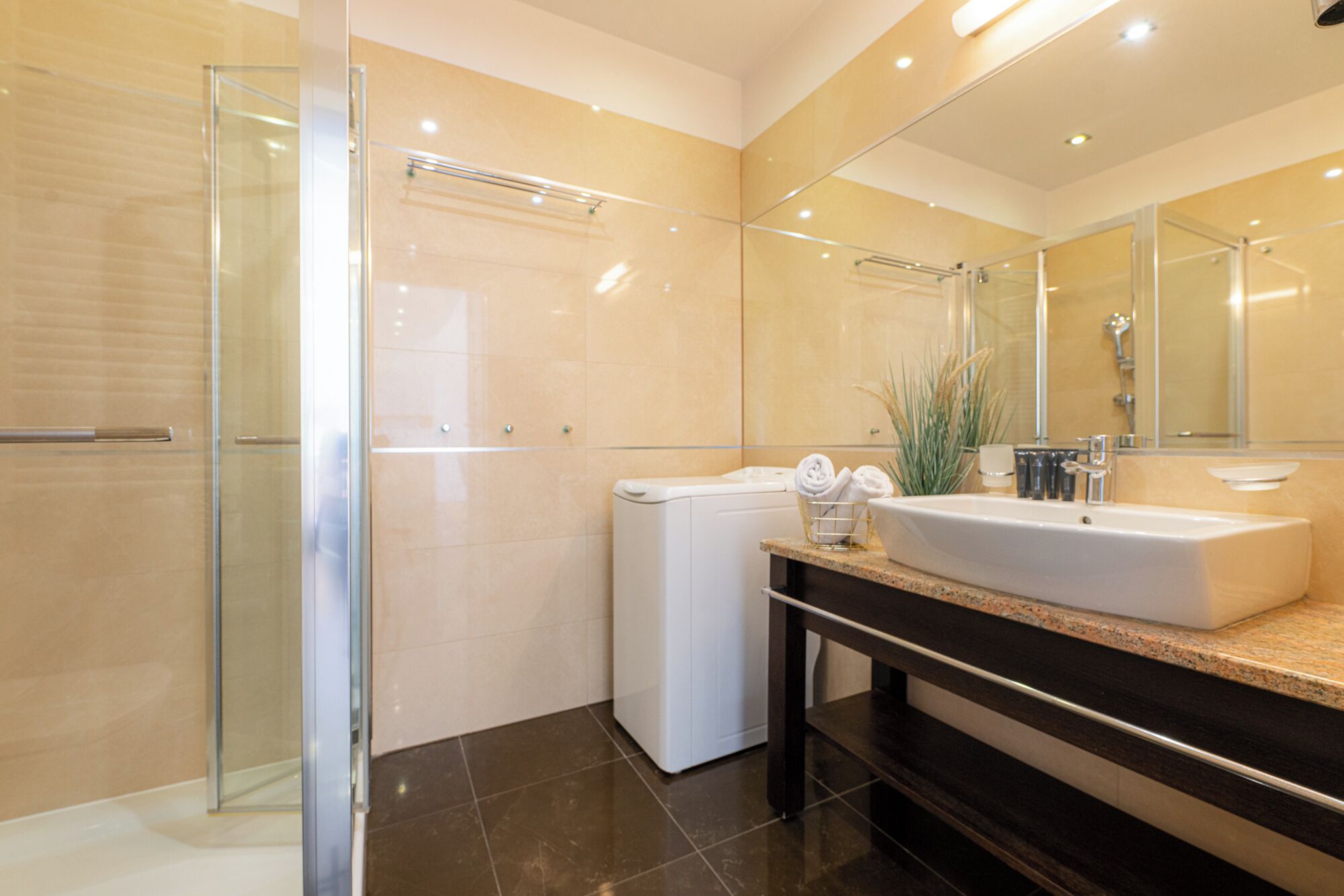 Un baño moderno con cabina de ducha de vidrio, lavadora blanca y lavabo con encimera de granito.