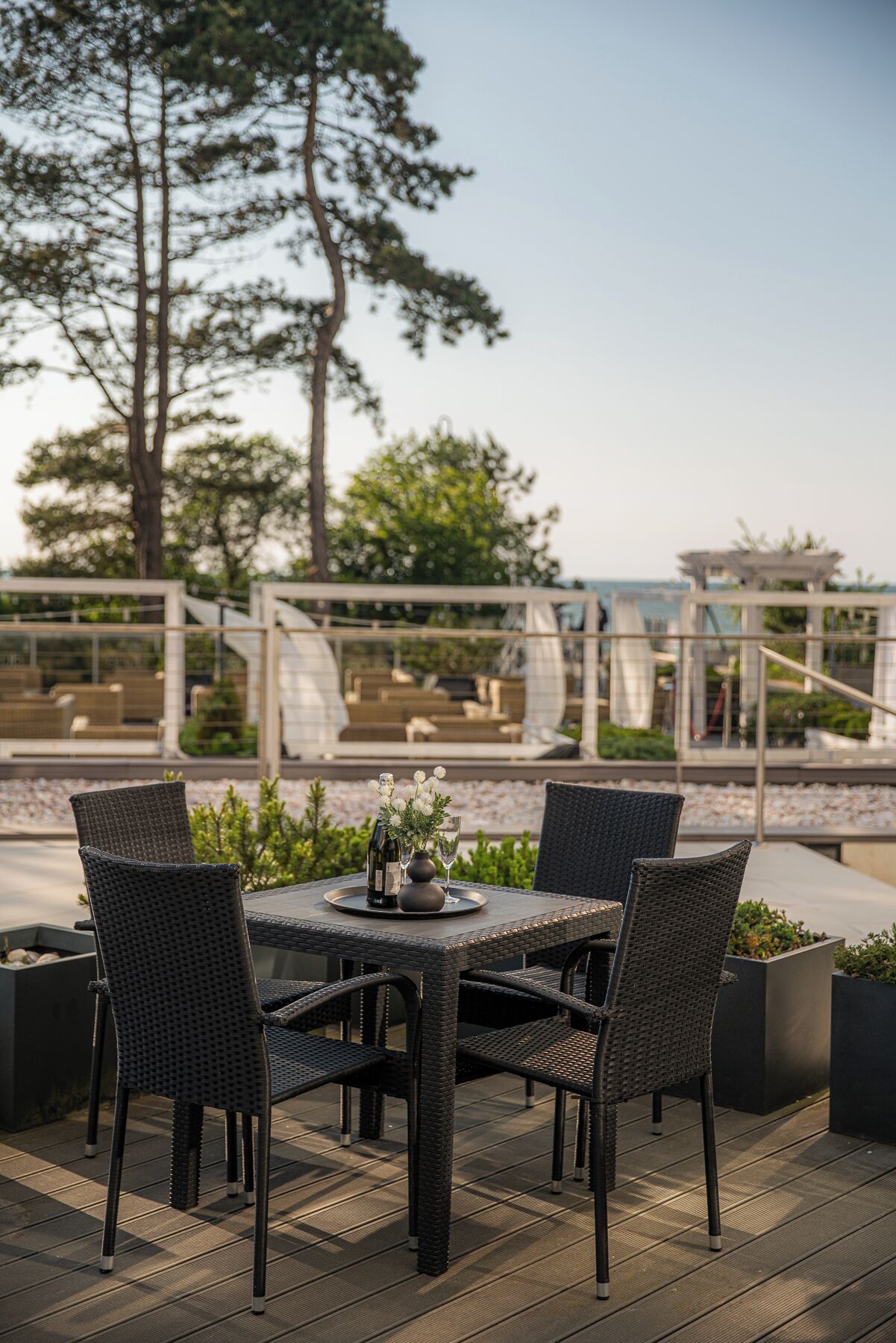 Un espace de restauration en plein air, avec des chaises et une table en osier, donnant sur une piscine et un bâtiment à la façade en verre.
