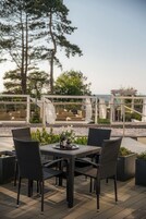 Et udendørs spiseområde med fletstole og et bord, med udsigt over en pool og en bygning med glasfacade.