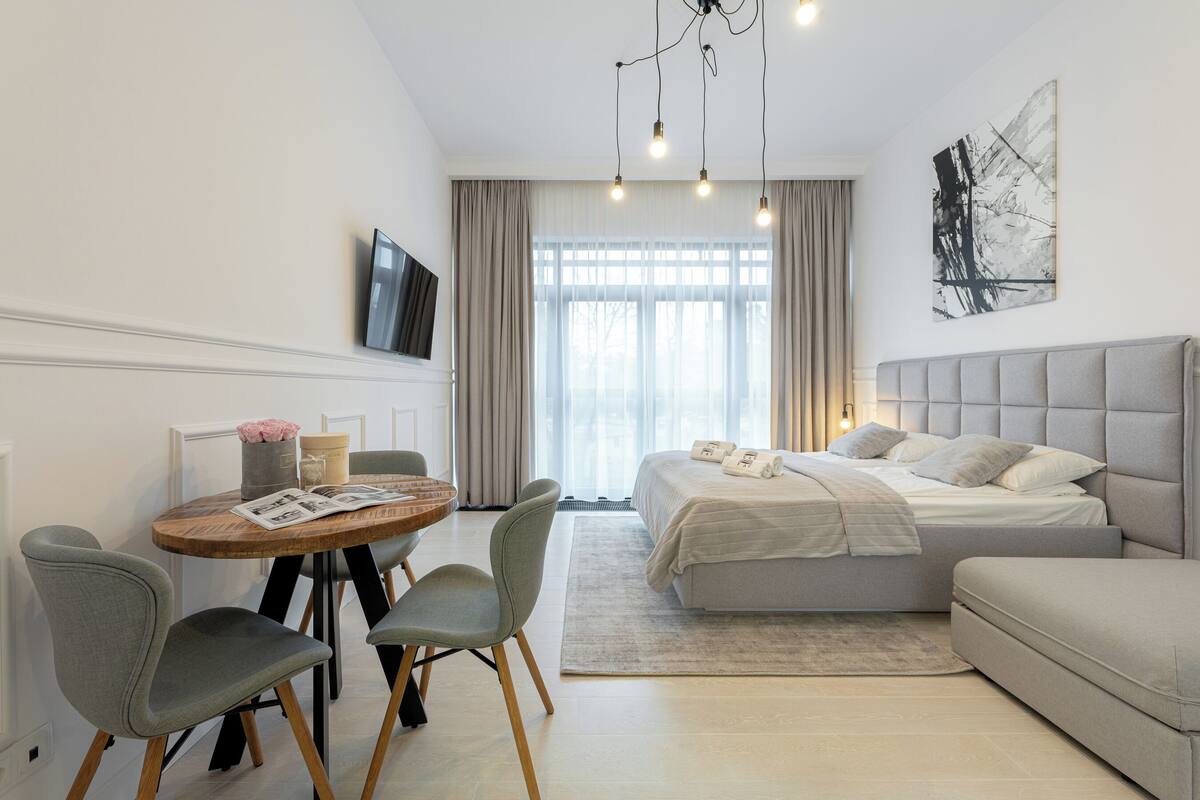 Un dormitorio moderno con cama, sofá, mesa de comedor con sillas y televisor en la pared.