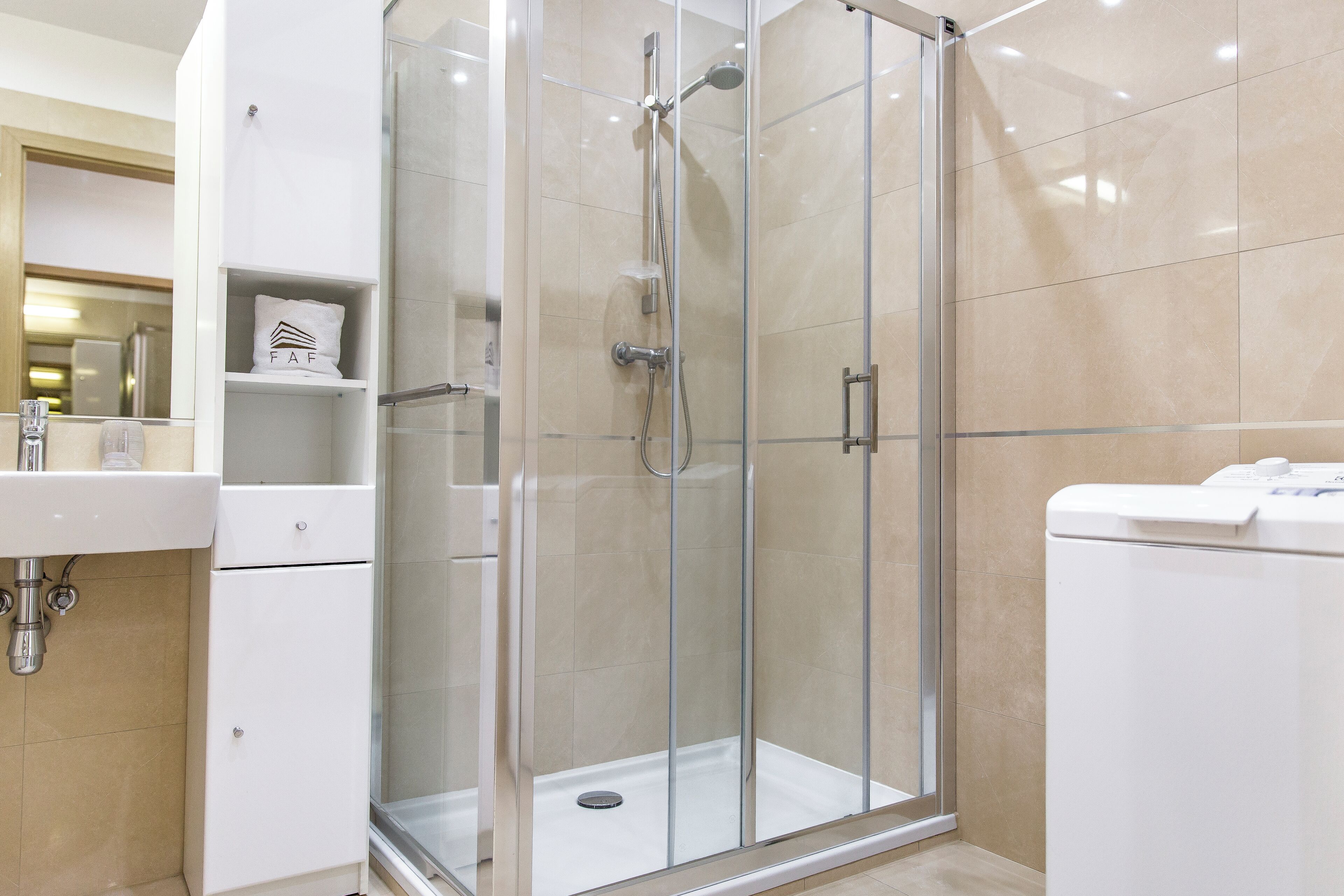 A modern bathroom with a glass-enclosed shower, a white sink, and a built-in washing machine.