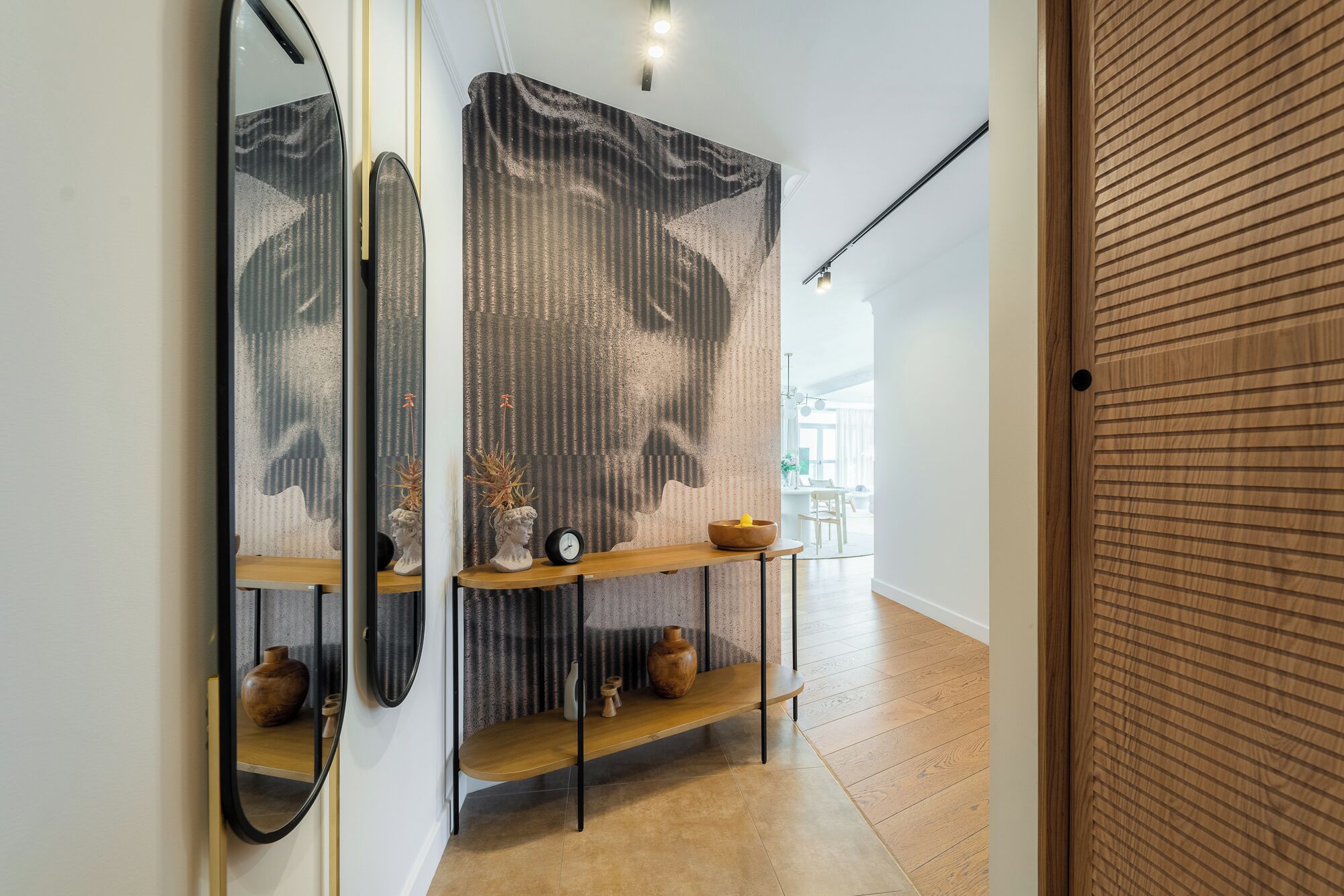 A hallway with a wooden floor, a console table with decorative items, a mirror, and a textured wall.
