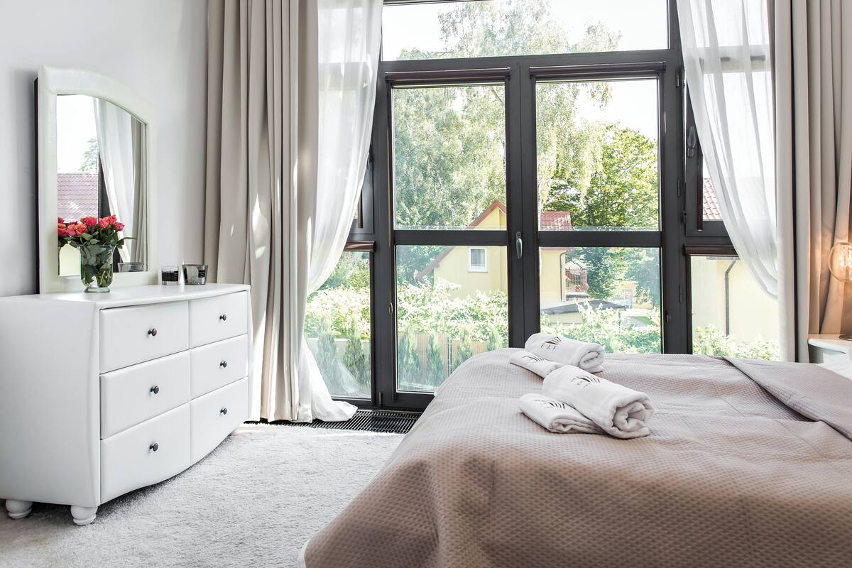 Un dormitorio con un ventanal grande, un aparador blanco y una cama bien hecha.