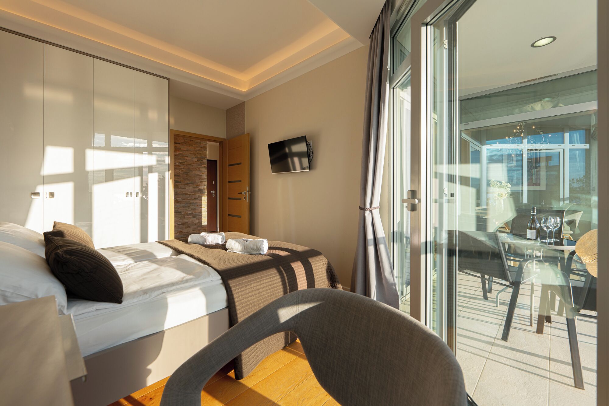 Une chambre d’hôtel comprenant un lit, une chaise, un bureau avec un plateau en verre et donnant sur le balcon extérieur.