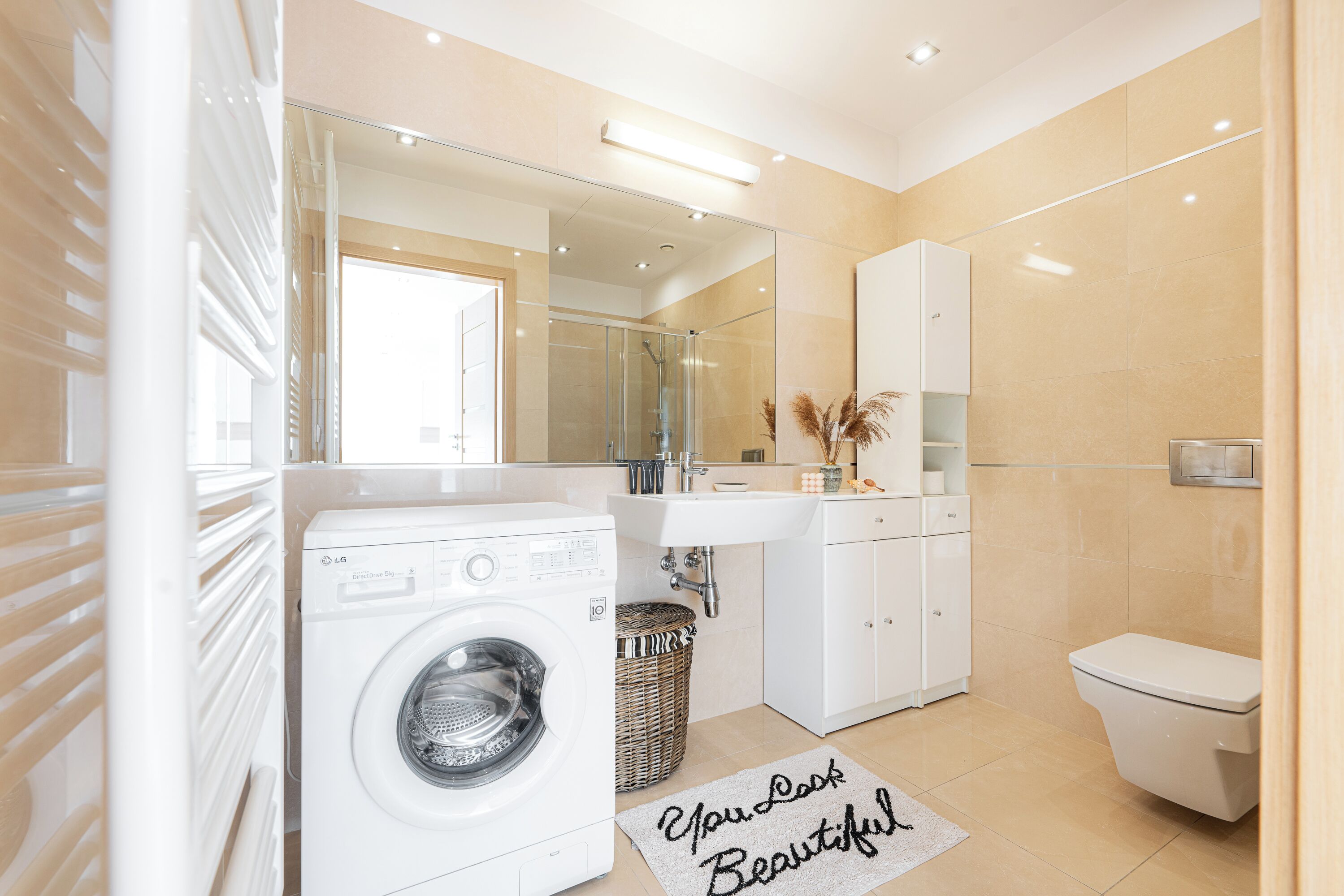 A modern bathroom with a washing machine, a sink, a toilet, and a mirror.