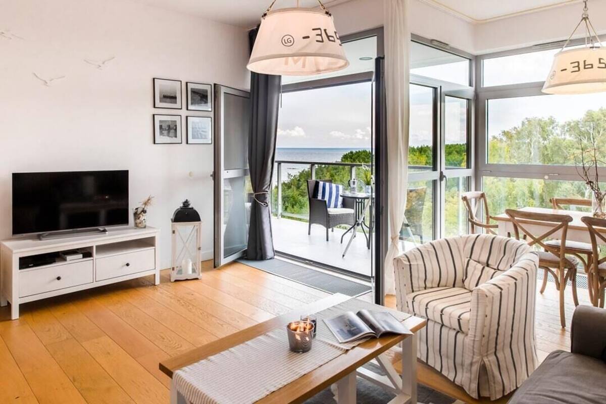 Una sala de estar moderna con televisor de pantalla plana, una mesa de centro de madera, un sillón a rayas y un balcón con vistas.