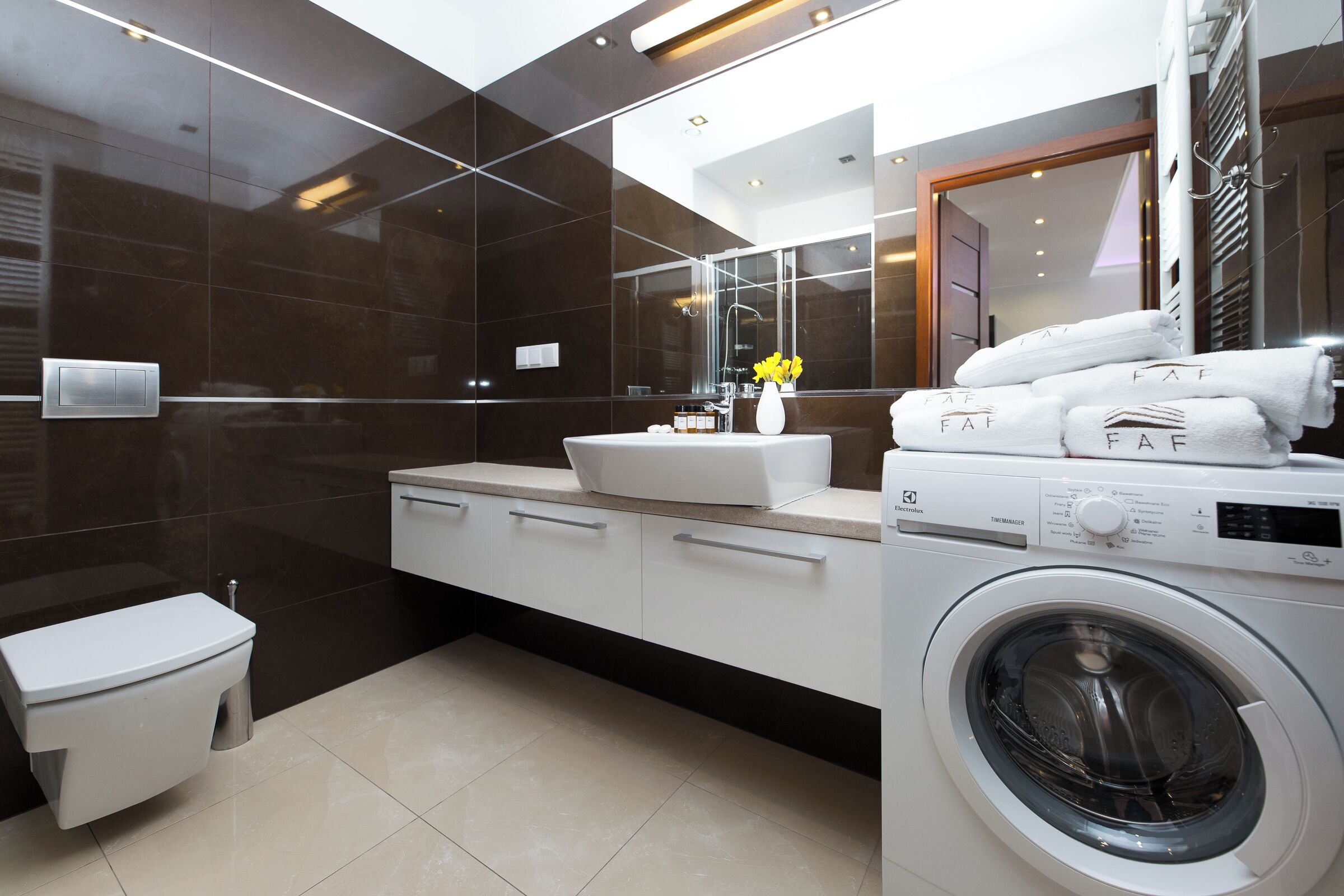 A modern bathroom with a large mirror, a washing machine, and a toilet.