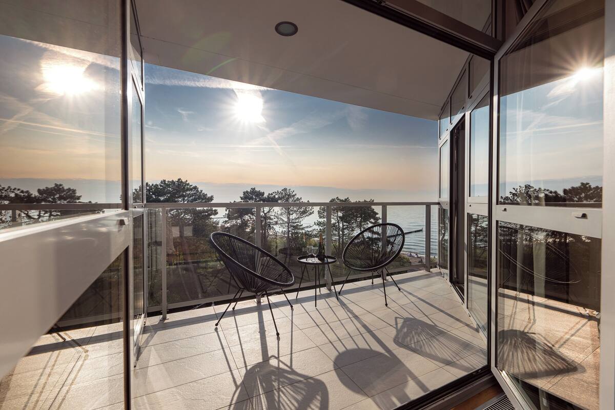 Un balcón con dos sillas y una mesa, con vistas a un paisaje de árboles y el mar.