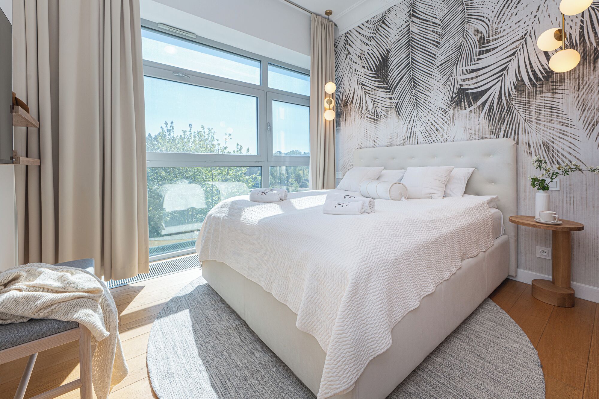Une chambre à coucher moderne avec un grand lit, une vue sur la verdure et un motif de feuilles tropicales sur le mur.