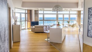 Un vaste espace de vie doté d’une grande fenêtre donnant sur la mer, d’un canapé moderne, d’une table à manger avec des chaises et d’un téléviseur.