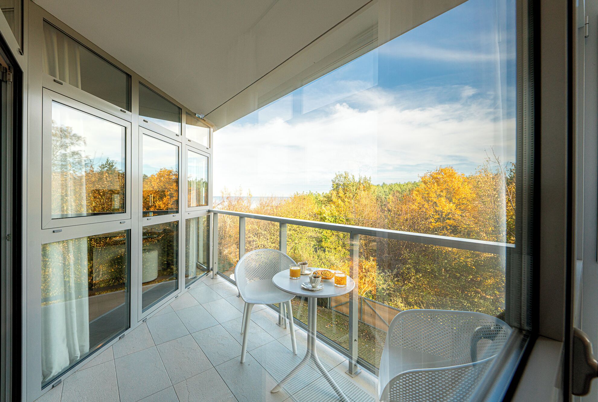 Un balcone con tavolo e sedie, da cui si apre una vista sugli alberi d'autunno.