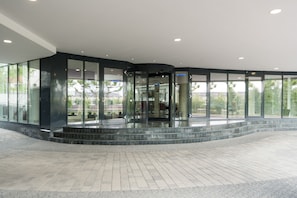 Un edificio moderno con una entrada de vidrio curva, suelo de baldosas y vistas del entorno.