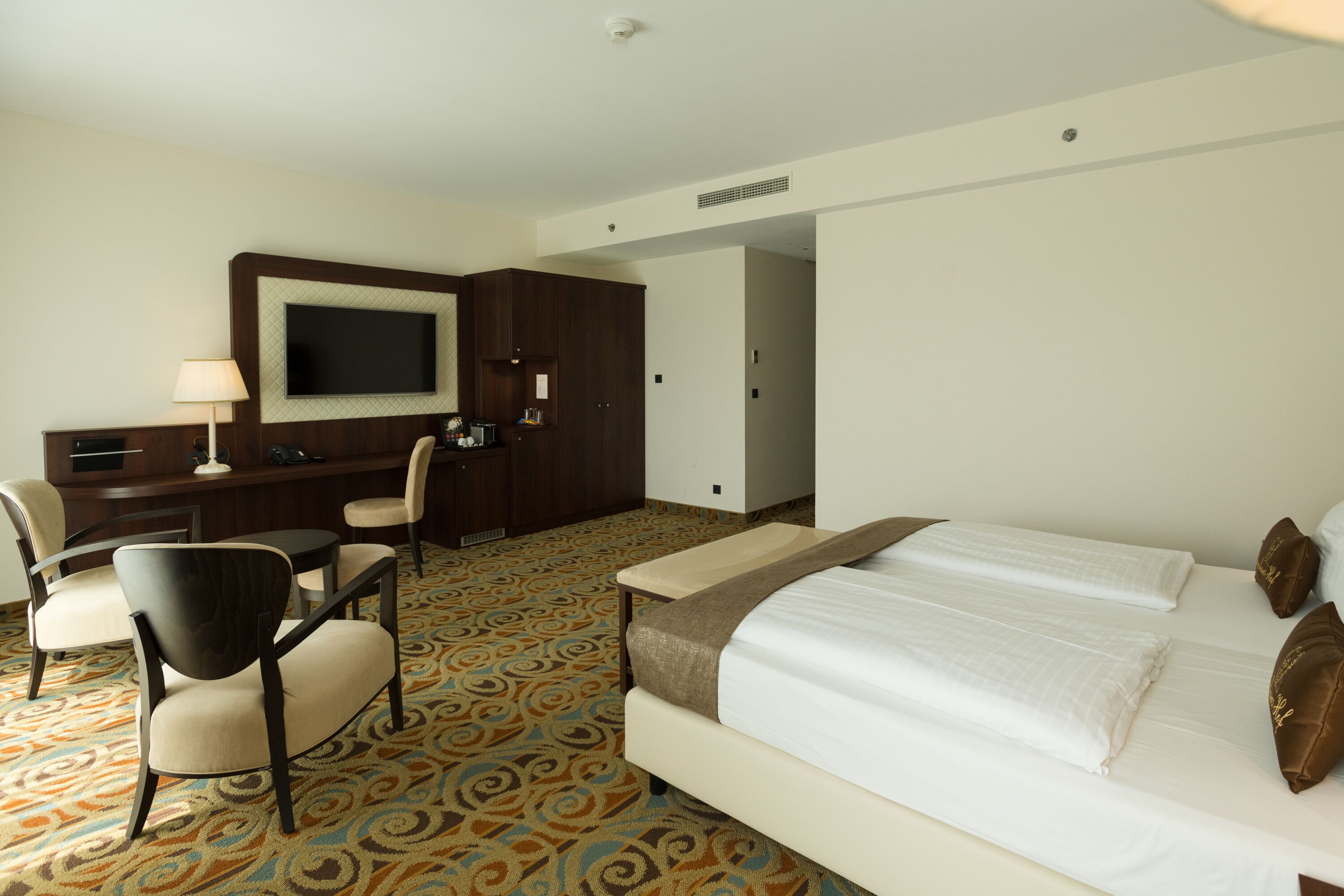 A hotel room with a bed, a desk, a chair, and a television.
