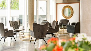 A modern lobby with a glass door leading outside, several grey upholstered chairs around a glass table, and a decorative mirror on the wall. - Hotel Schopenhauer Hof (Frankfurt)