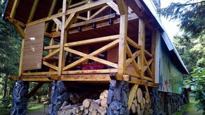 Una cabaña de madera con balcón, cimientos de piedra y una pila de leña.
