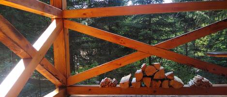 A wooden cabin with a sloped roof, wooden beams, and a view of a forest.